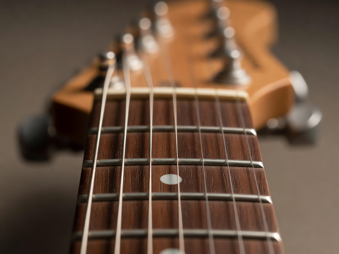 Close-up of guitar frets and strings with the headstock blurred in shallow focus